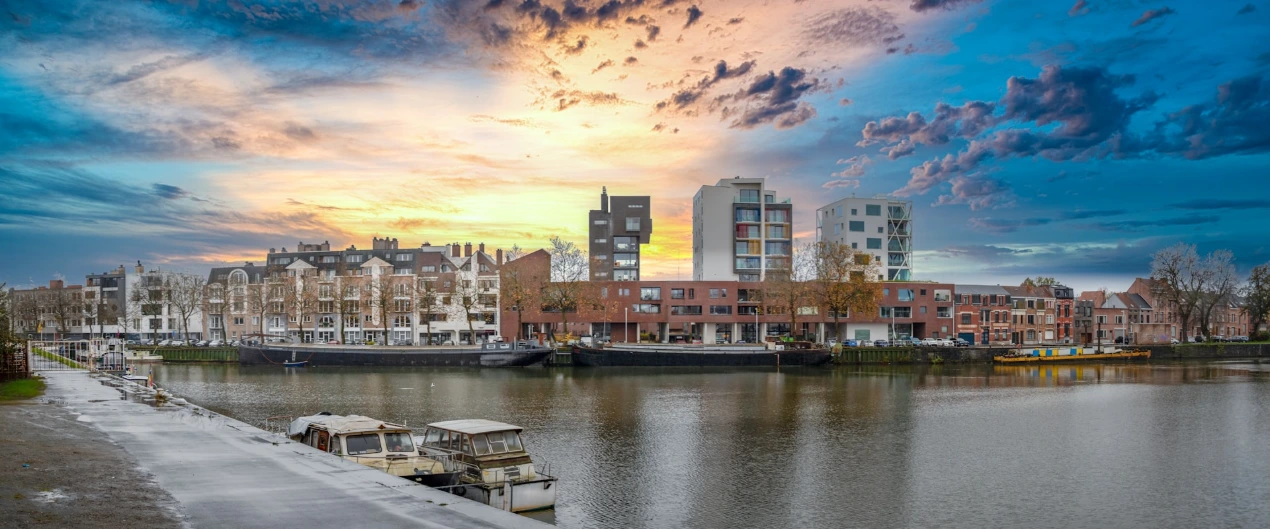 Cityscape by a river under a cloudy sky.